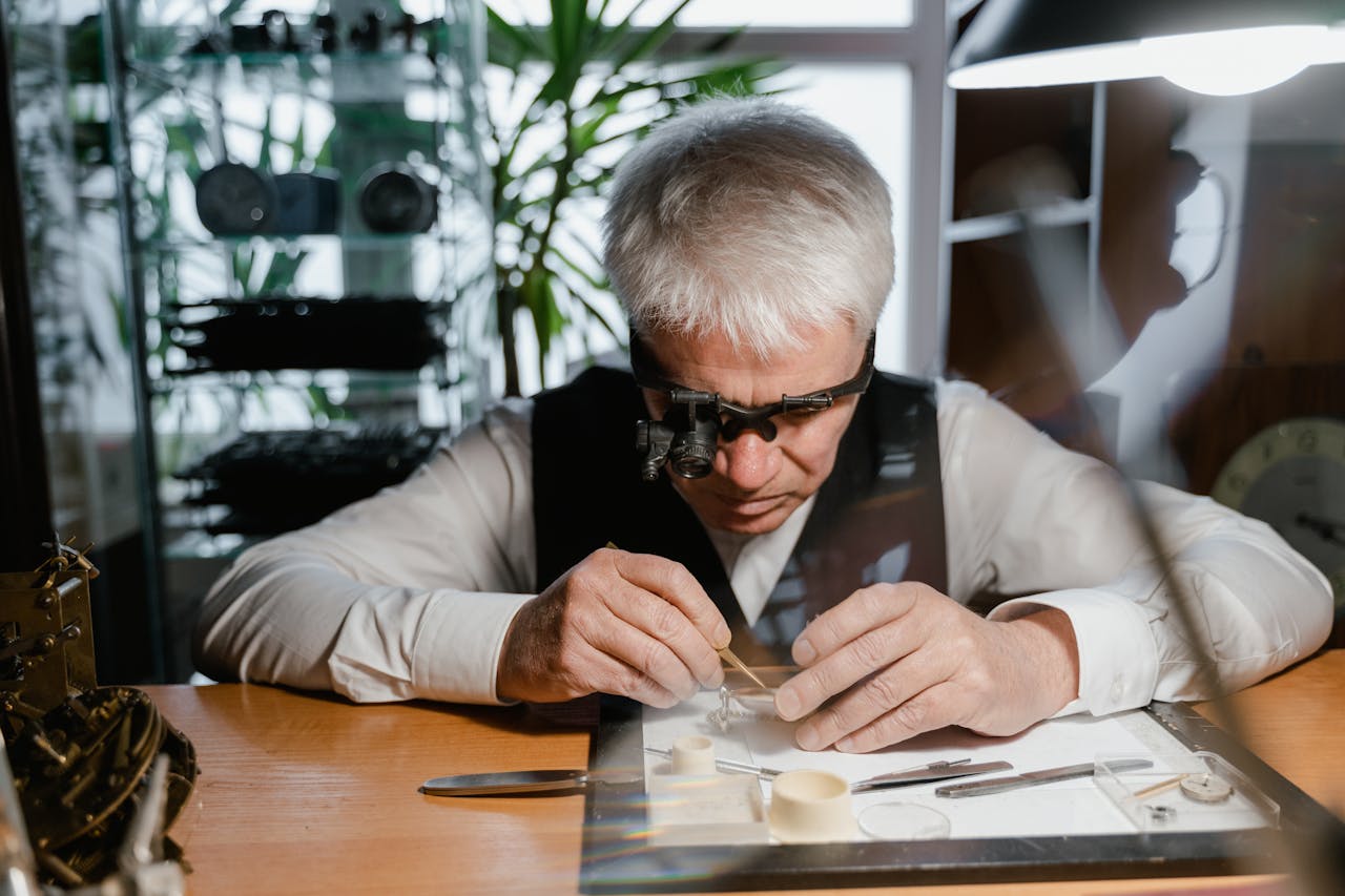 Senior watchmaker focuses intently on intricate repair work using specialized tools in a workshop.